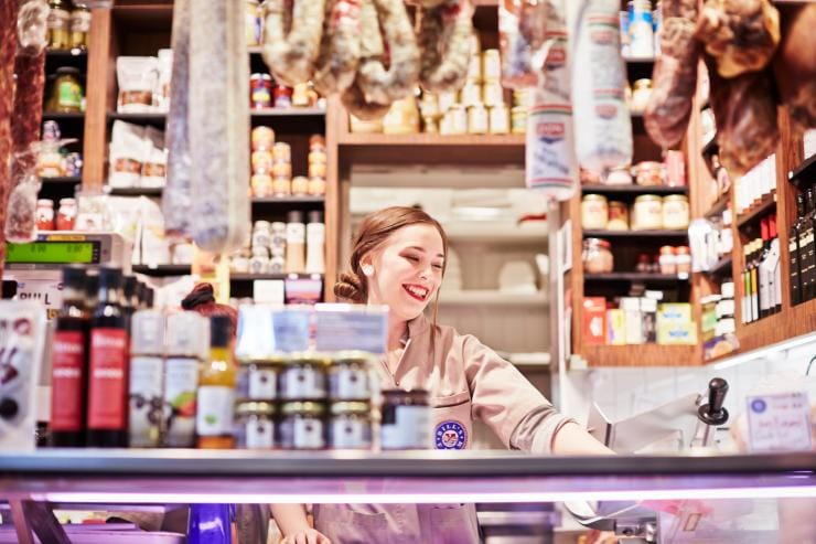 A woman standing behind the counter of a deli stocked with meat and preserves at Queen Victoria Market, Melbourne, Victoria © Ewen Bell A woman standing behind the counter of a deli stocked with meat and preserves at Queen Victoria Market, Melbourne, Victoria © Ewen Bell