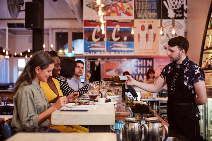 Two friends seated at a colourful bar, smiling as a bartender fills their glasses at Chin Chin, Melbourne, Victoria © Rebecca Newman Two friends seated at a colourful bar, smiling as a bartender fills their glasses at Chin Chin, Melbourne, Victoria © Rebecca Newman