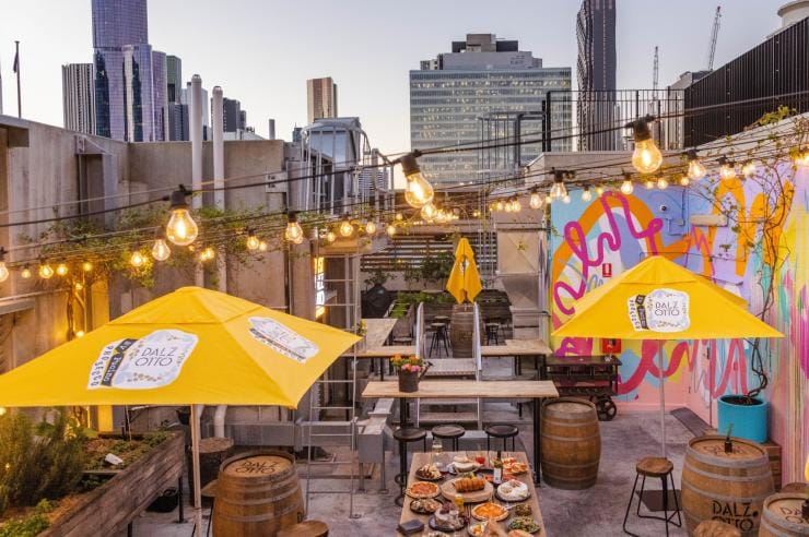 Bright yellow umbrellas and a colourful mural beneath strings of warm-hued light bulbs on the Rooftop at QT, Melbourne, Victoria © QT Melbourne Bright yellow umbrellas and a colourful mural beneath strings of warm-hued light bulbs on the Rooftop at QT, Melbourne, Victoria © QT Melbourne
