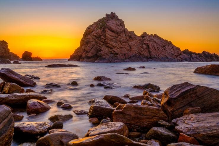 Sunset over the formation of Sugarloaf Rock in the calm ocean with rocks lining the shoreline in Leeuwin-Naturaliste National Park, Western Australia © Tourism Western Australia