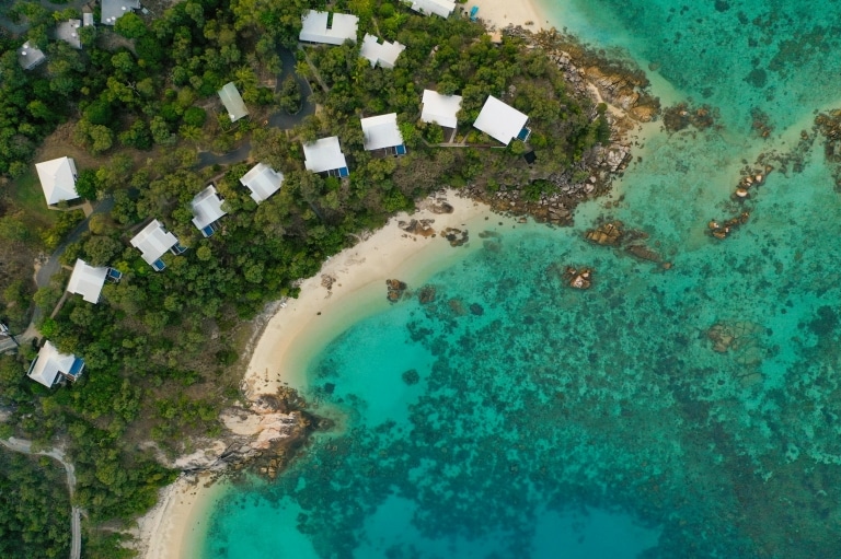Aerial view over Lizard Island Resort accommodation amid the trees on the white sandy coastline of Lizard Island, leading to clear blue ocean in Queensland © Tourism and Events Queensland