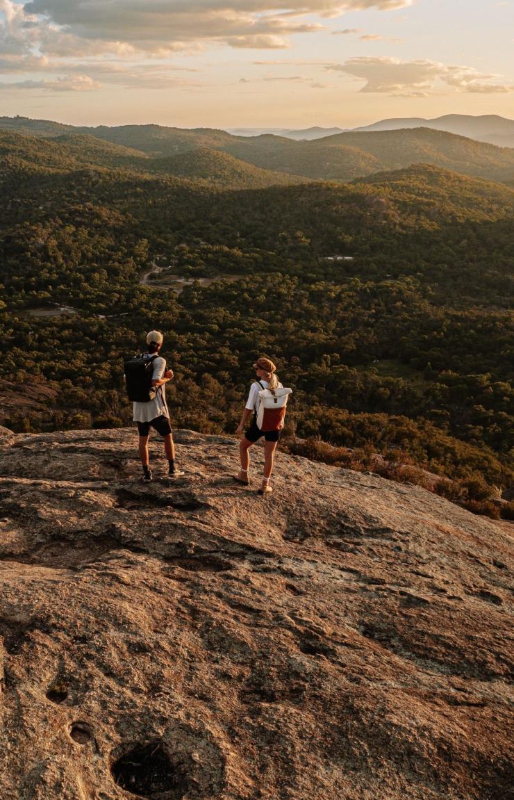 Two hikers stand atop a rocky outcrop looking over Girraween National Park, Queensland Country, Queensland © Tourism Australia