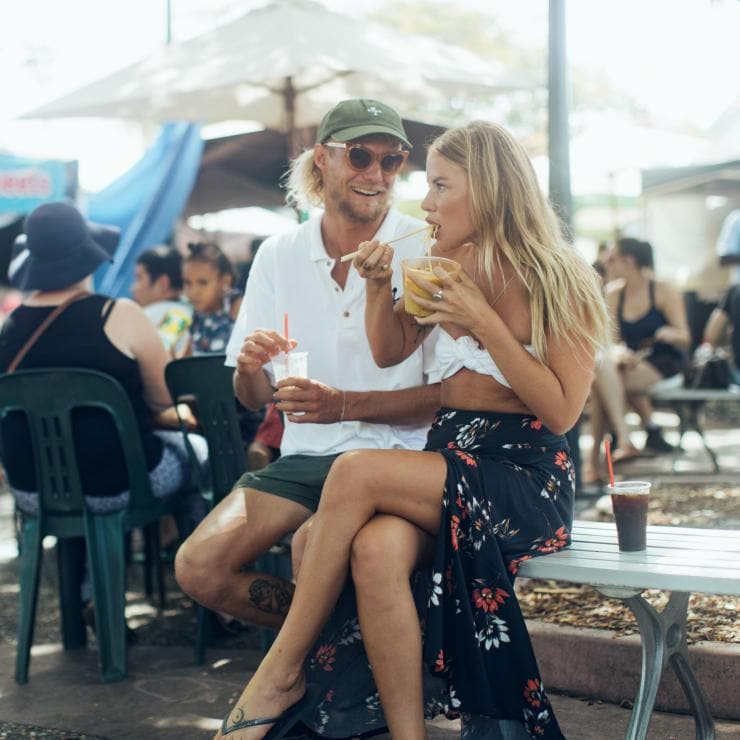 A couple eating Street food at Parap Village Markets, Darwin Northern Territory, outdoors on a sunny day. © Tourism Northern Territory
