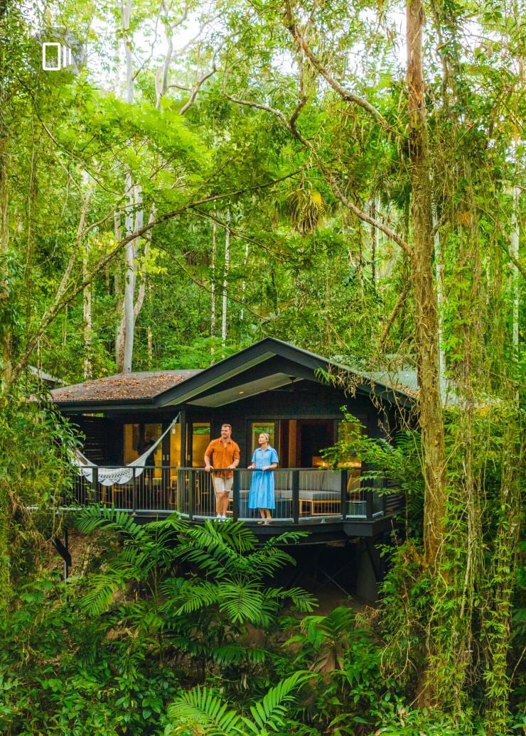 A man and woman standing on the balcony of a villa with a hammock surrounded by lush green trees, Queensland © Tourism and Events Queensland