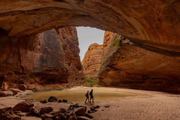 Two people hiking through an enormous, rocky orange gorge, Cathedral Gorge, Purnululu National Park, Western Australia © Tourism Australia