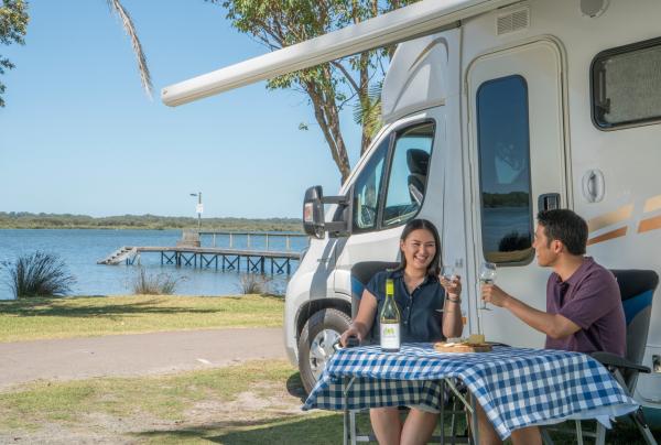 Couple profitant d'un verre de vin et de la vue sur l'eau depuis leur fourgon aménagé dans le BIG4 Koala Shores Port Stephens Holiday Park © Destination NSW