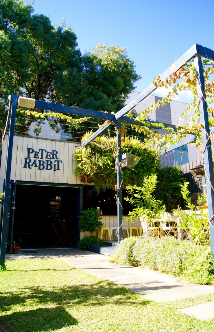 Un jardin luxuriant avec un espace pour s'asseoir en plein air devant un café et un panneau arborant Peter Rabbit, Adélaïde, Australie du Sud © James McIntyre