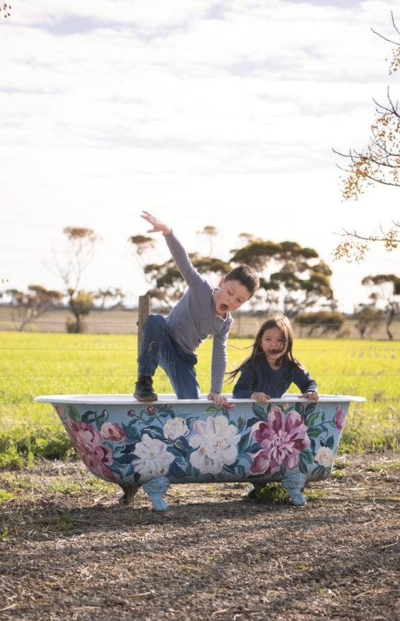 Un petit garçon et une petite fille jouent dans une baignoire de plein-air avec des fleurs à Redwing Farm, Yorke Peninsula, Australie du Sud © Tourism Australia 