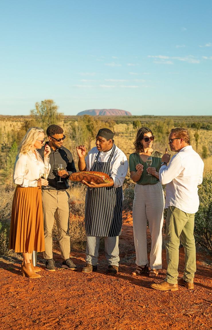 Un groupe de personnes et un chef goûtant des plats avec le site d'Uluru en arrière-plan, Tali Wiru, Yulara, Territoire du Nord © Tourism Australia