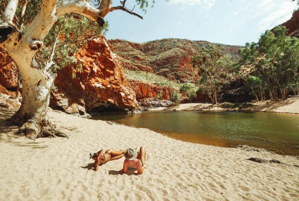 Deux amis se détendent sur le sable au bord de l'eau à Ormiston Gorge © Tourism NT/Jackson Groves
