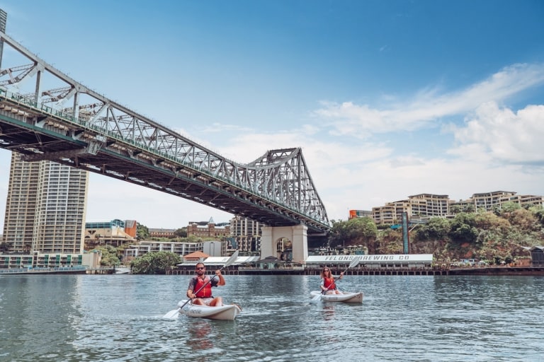 Un homme et une femme faisant du kayak avec Riverlife sur le fleuve Brisbane River et passant sous le Story Bridge avec Howard Smith Wharves en arrière-plan à Brisbane, Queensland © Tourism and Events Queensland