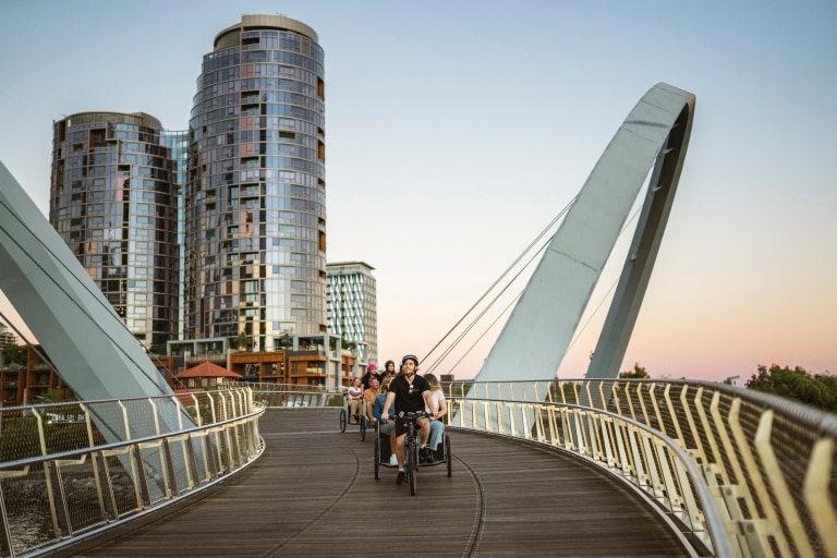 Groupe de touristes profitant d'un trajet en pousse-pousse sur un pont le soir avec Peddle Perth, Perth, Australie Occidentale © Tourism Australia