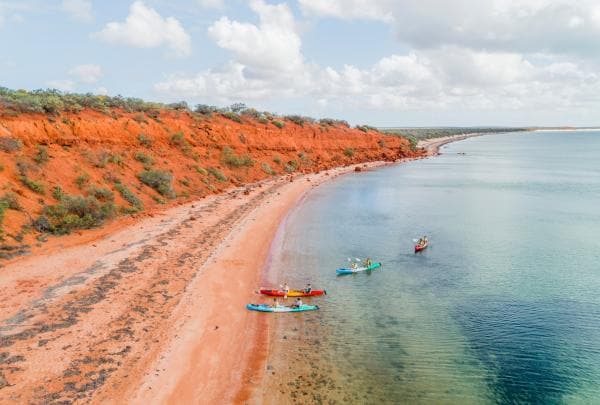 Une vue aérienne d'un groupe de personnes faisant du kayak dans des eaux cristallines à côté de falaises orange vif lors d'un circuit avec Wula Gura Nyinda Eco Cultural Adventures, Coral Coast, Australie Occidentale © Tourism Western Australia
