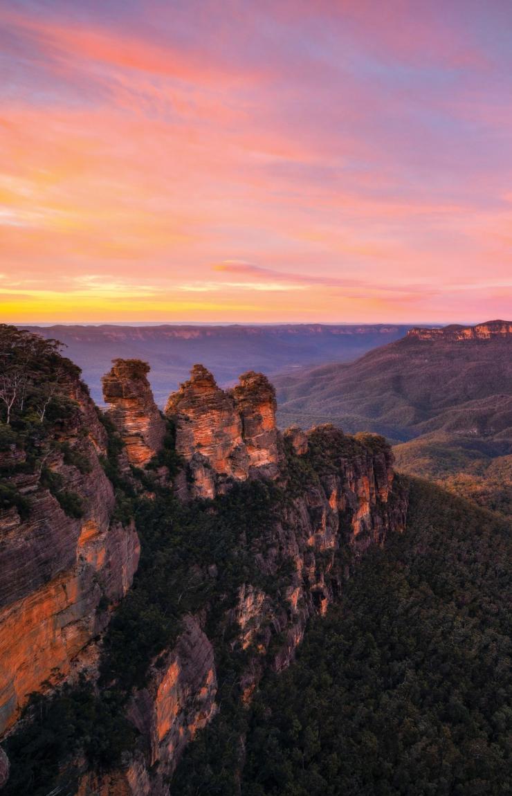 Three rock formations towering over a lush green valley during sunset, Three Sisters, Blue Mountains, New South Wales © Daniel Tran/Destination New South Wales