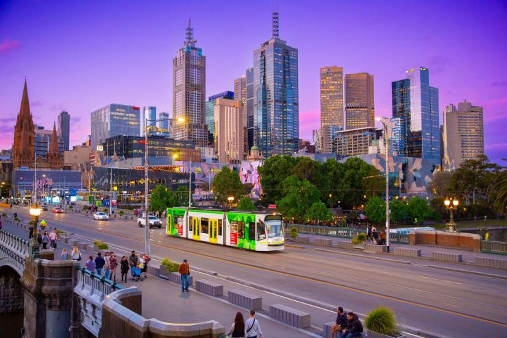 Sebuah trem dan pejalan kaki di Jembatan Princes Melbourne pada waktu senja, dengan cakrawala kota dan langit ungu di latar belakang, Victoria © Tourism Australia