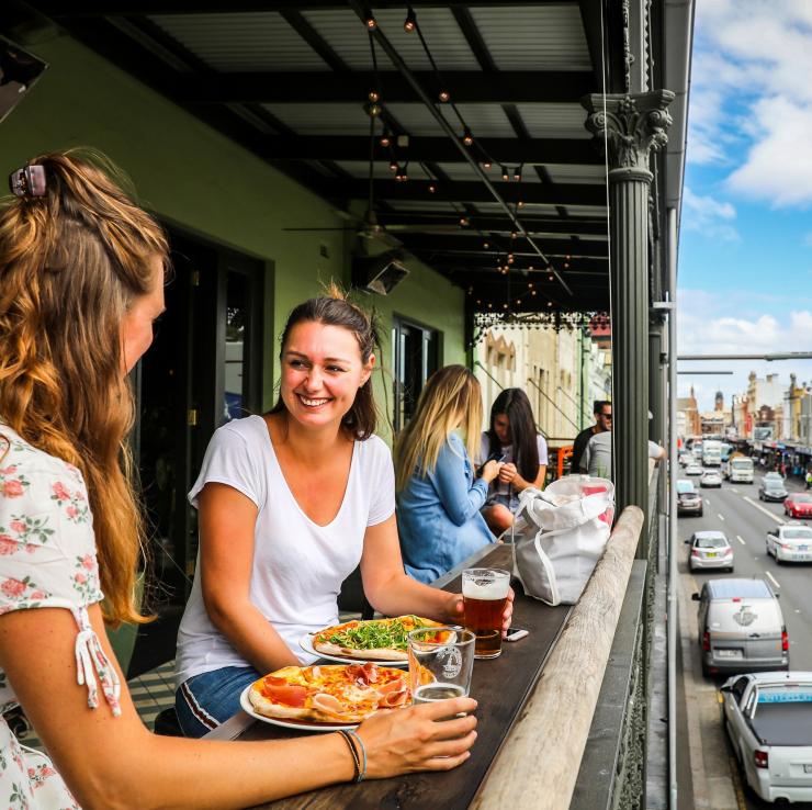 Sekelompok teman menikmati pizza dan minuman di balkon Newtown Hotel © City of Sydney/Katherine Griffiths