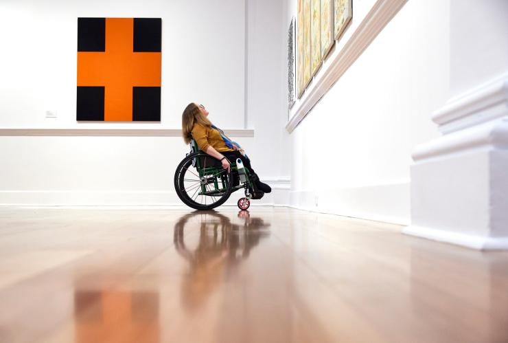 Seorang wanita yang duduk di kursi roda mengagumi seni di Geelong Gallery, Geelong, Victoria © Tourism Australia