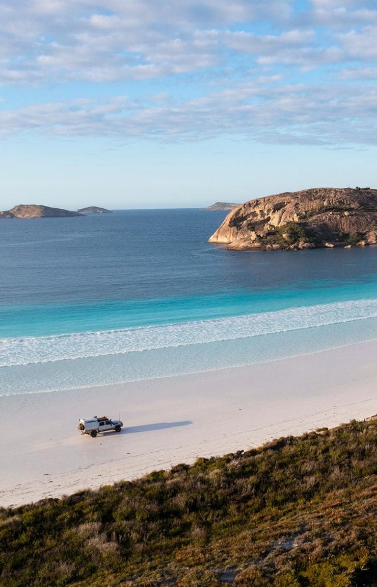 Pemandangan dari udara mobil 4WD melaju di pantai pasir putih dengan air biru cerah di Lucky Bay, Esperance, Western Australia © Tourism Western Australia