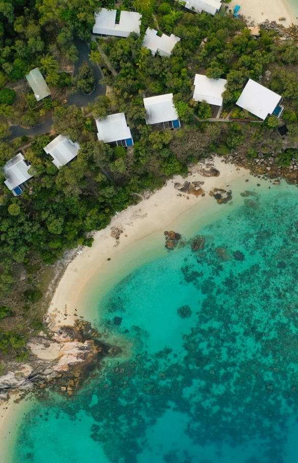 Pemandangan udara di atas akomodasi Lizard Island Resort di tengah pepohonan di pesisir pantai berpasir putih Lizard Island, yang mengarah ke samudra biru jernih di Queensland © Tourism and Events Queensland
