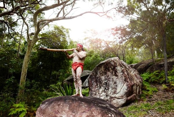 Pria memainkan didgeridoo di atas batu, Pretty Beach House, Bouddi National Park, NSW © Pretty Beach House