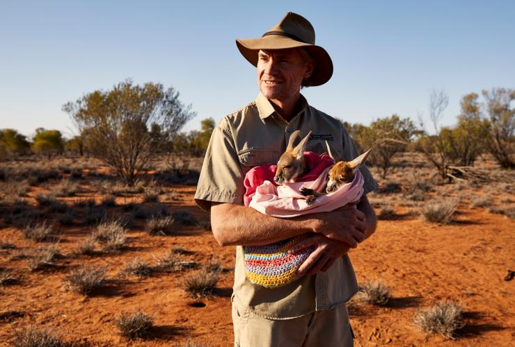 Chris ‘Brolga’ Barns memegang bayi kanguru di The Kangaroo Sanctuary © Tourism Australia