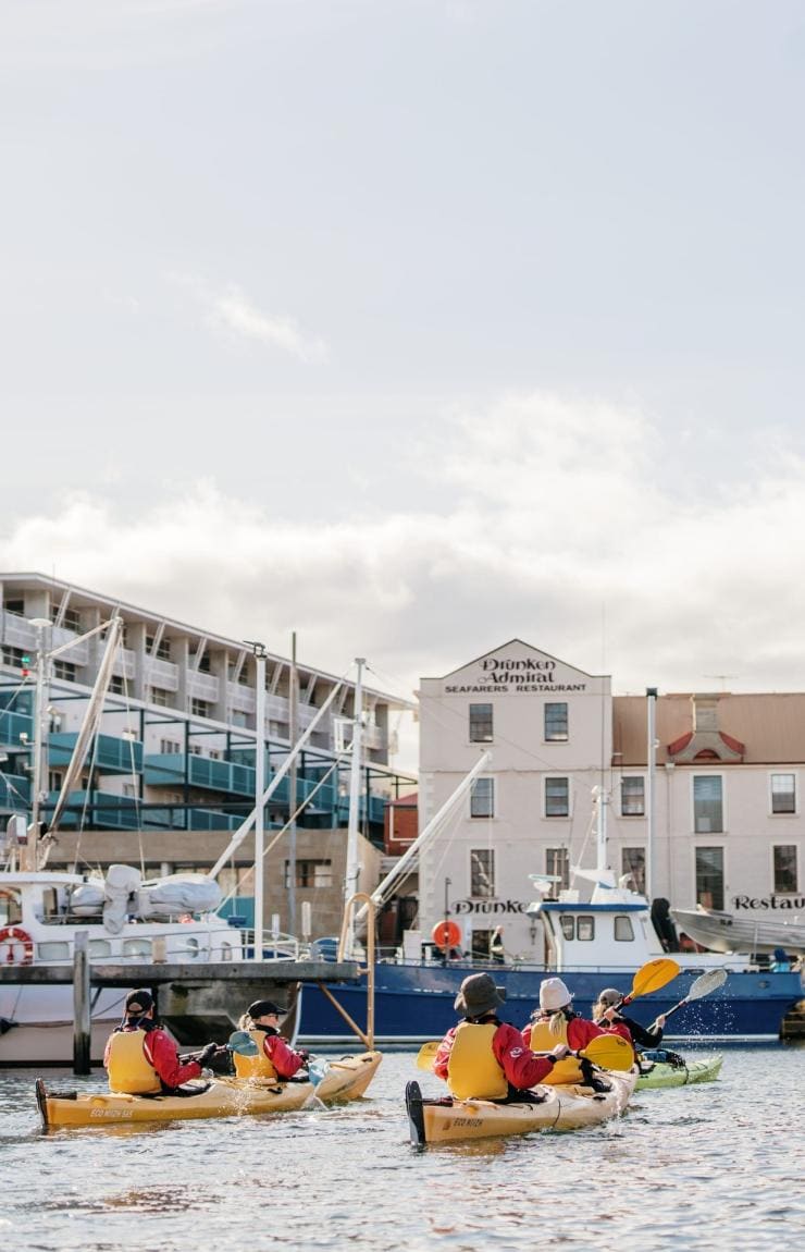 Sekelompok orang mendayung kayak kuning di antara perahu di marina bersama Roaring 40s Kayaking di Hobart, Tasmania © Tourism Australia