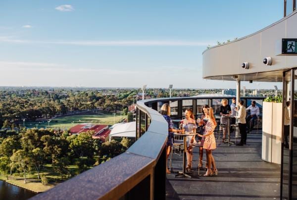 Gruppo di amici che sorseggiano un drink intorno a un tavolo su una terrazza affacciata sui sobborghi e sul bushland al SOL Rooftop, Adelaide, South Australia © Meaghan Coles