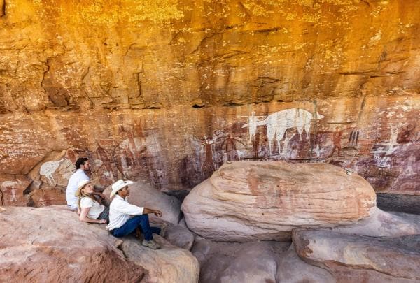 Due viaggiatori seduti insieme a una guida aborigena ammirano l'arte rupestre con Jarramali Rock Art Tours, Cook, Queensland © Tourism Australia