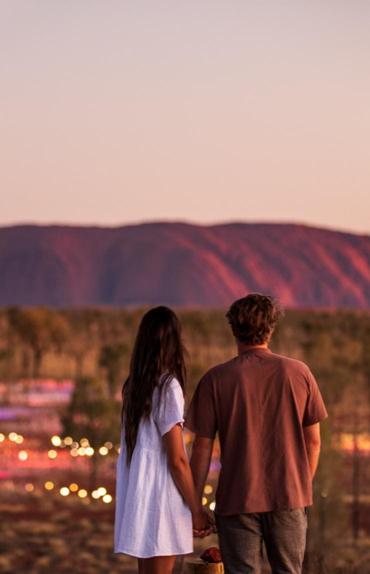 Coppia davanti a Uluru e all'installazione Field of Light durante il tramonto nel Northern Territory © Tourism NT/The Salty Travellers