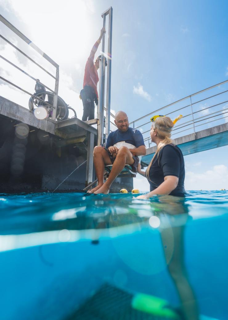 クイーンズランド州、グレートバリアリーフ、クイックシルバー・クルーズの船上リフトを使って海に降りる足の不自由な男性 © Tourism and Events Queensland
