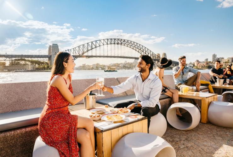 ニュー・サウス・ウェールズ州、シドニーのオペラ・バーでハーバーを眺めながら食事とドリンクを楽しむカップル © Destination NSW
