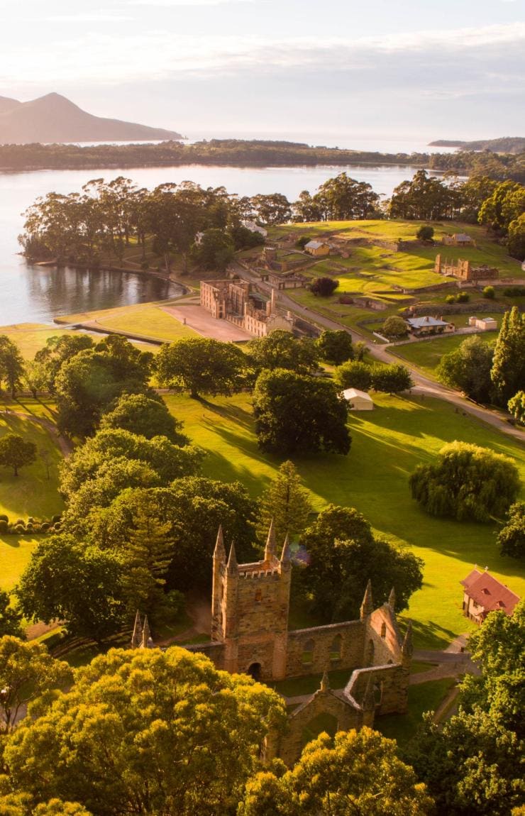 タスマニア州、ポート・アーサー、太陽の光の中、穏やかな青い海と緑地に囲まれ佇むポート・アーサー史跡の空撮 © Alastair Bett 