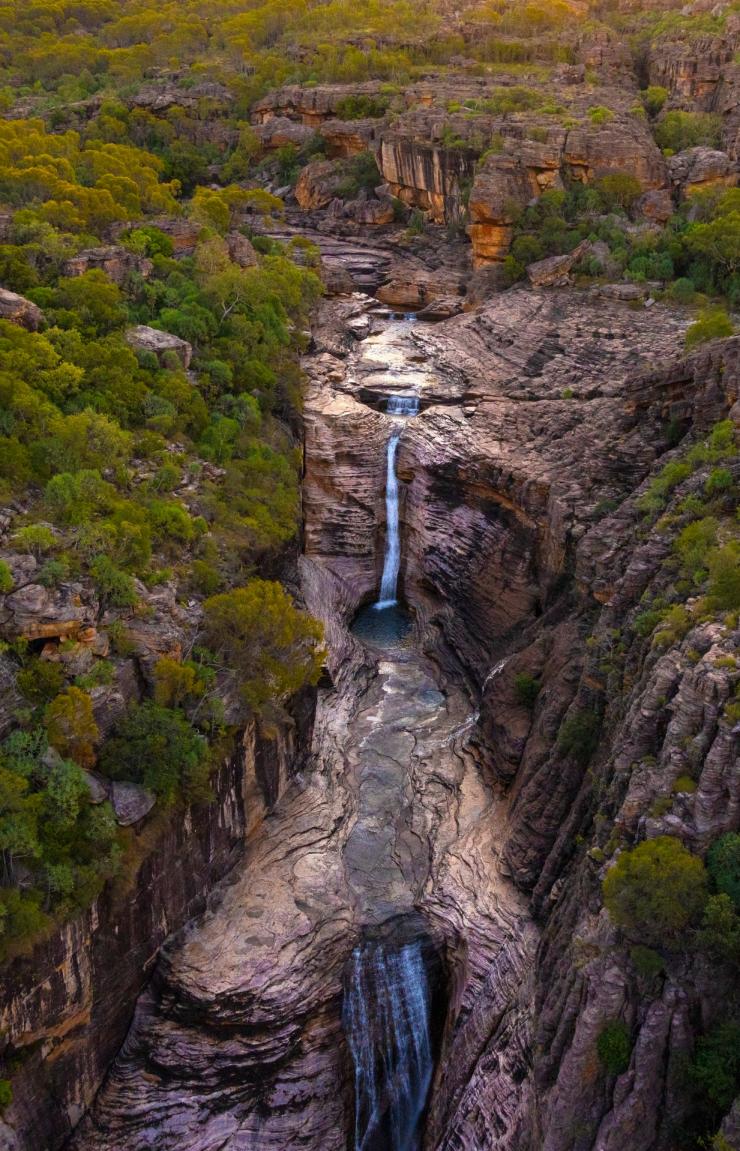 ノーザンテリトリー、カカドゥ国立公園のジム・ジム・フォールズと一帯に広がる赤い岩と緑地の空撮 © Sean Scott