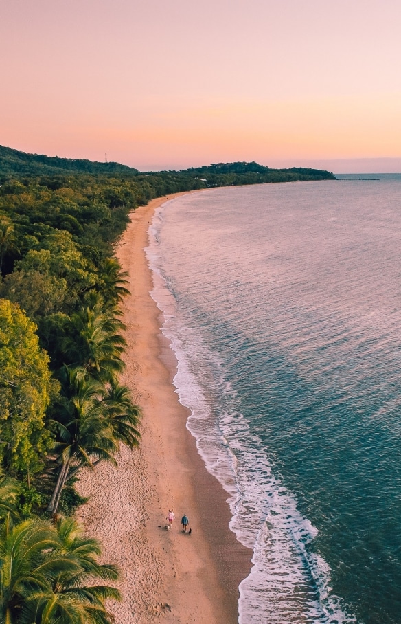 クイーンズランド州、ケアンズ、熱帯雨林と海を隔てるクリフトン・ビーチの長い砂浜を歩く2人の人物を捉えた空撮 © Tourism and Events Queensland