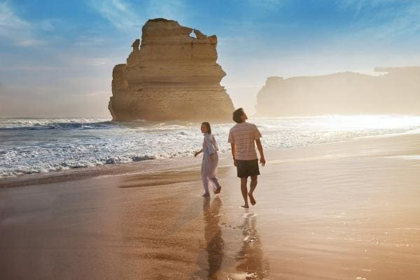 Couple walking along the beach with the twelve apostles in the background © Tourism Australia