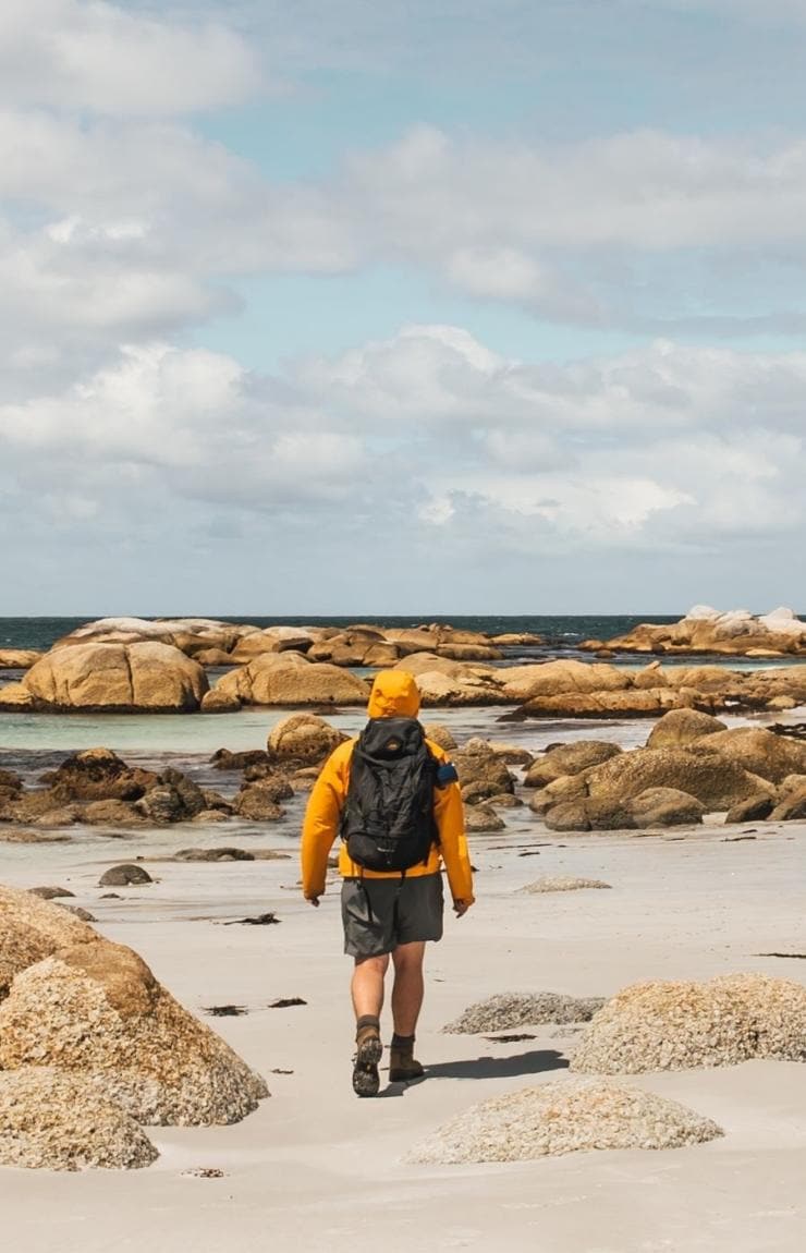 크고 주황색 바위가 있는 새하얀 해변을 따라 걷는 사람