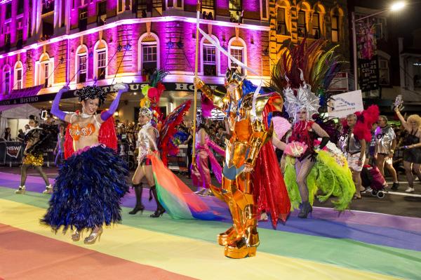 A group of dancers dressed in elaborate, colourful outfits performing on a street painted with a rainbow at Sydney Gay and Lesbian Mardi Gras, Sydney, New South Wales © Destination NSW