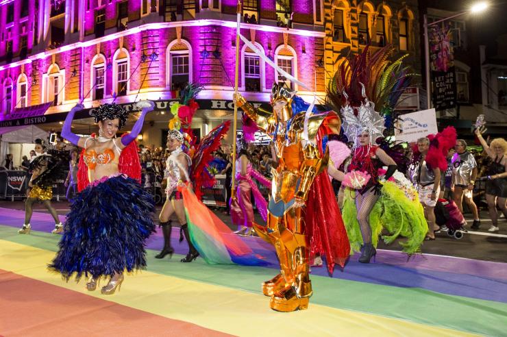 A group of dancers dressed in elaborate, colourful outfits performing on a street painted with a rainbow at Sydney Gay and Lesbian Mardi Gras, Sydney, New South Wales © Destination NSW