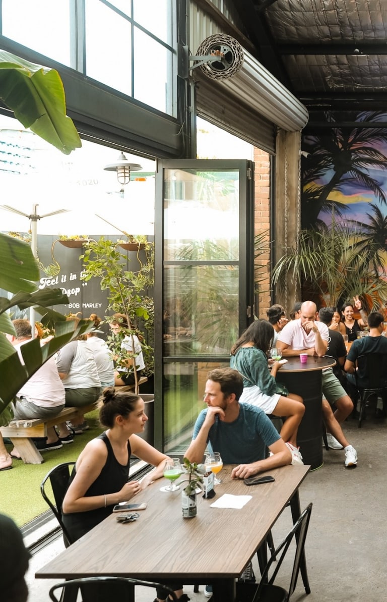 A crowd of people sitting around long tables in a brewery with a colourful mural. at One Drop Brewing, Botany, Sydney, New South Wales © One Drop Brewing Co. 