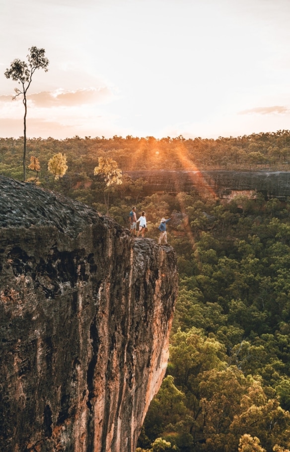 An Aboriginal tour guide and two guests standing on a rocky outcrop overlooking green bushland during a tour with Jarramali Rock Art Tours, Tropical North Queensland, Queensland © Tourism Tropical North Queensland 