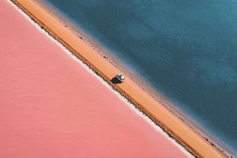 Aerial view of a car driving on a dirt road next to the bright pink Lake Macdonnell, Eyre Peninsula, South Australia © Lyndon O'Keefe