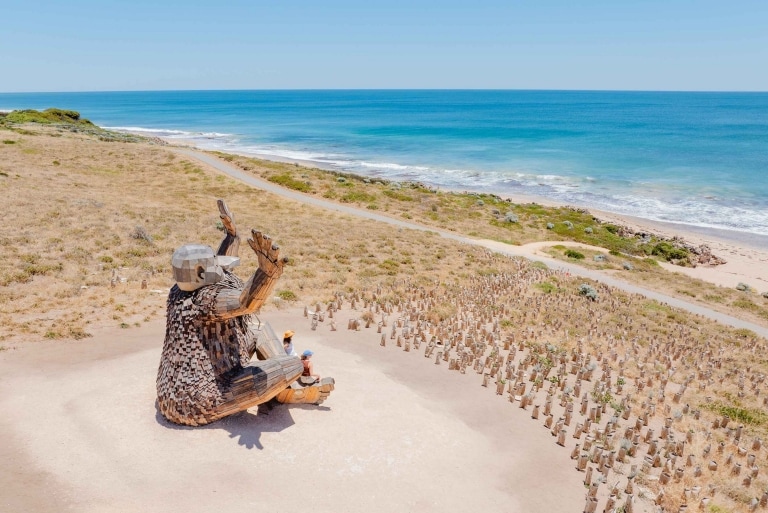 Góc nhìn từ trên cao về những du khách đang đứng bên cạnh bức tượng người khổng lồ hướng ra biển – Santi Ikto-Giants of Mandurah của Thomas Dambo, Thành phố Mandurah, Tiểu bang Tây Úc © Visit Mandurah