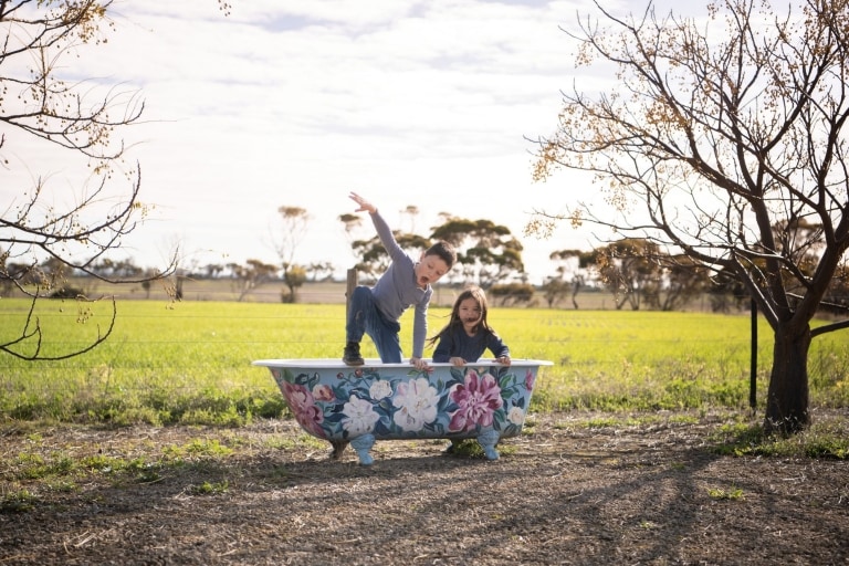 A young boy and girl play in an outdoor bathtub painted with flowers at Redwing Farm, Yorke Peninsula, South Australia © Tourism Australia 