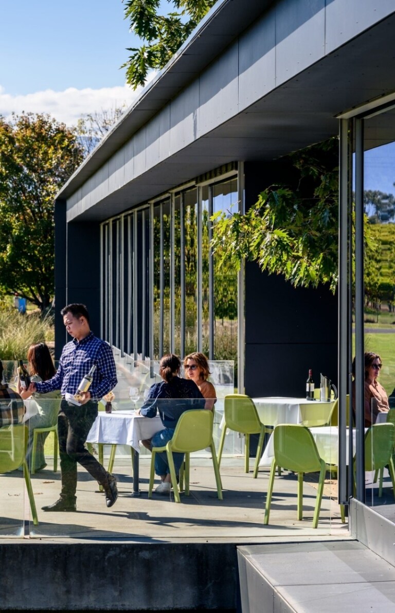 People dining and drinking wine on a terrace overlooking a lush green vineyard, Oakridge Wines, Yarra Valley, Victoria © Visit Victoria