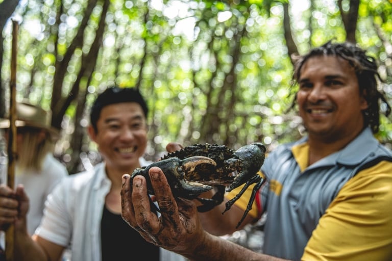 An Indigenous guide holding up a mud crab as a tour participant smiles behind him, Walkabout Cultural Adventures, Daintree Rainforest, Queensland © Tourism and Events Queensland