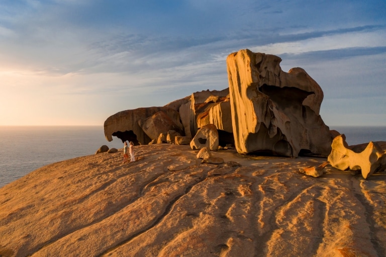 Hai người dạo bước bên những khối đá kỳ vĩ của Remarkable Rocks khi hoàng hôn buông xuống, phía sau là đại dương trên Đảo Kangaroo, tiểu bang Nam Úc © South Australian Tourism Commission