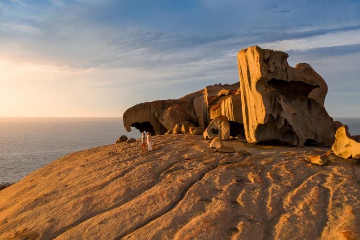 Hai người dạo bước bên những khối đá kỳ vĩ của Remarkable Rocks khi hoàng hôn buông xuống, phía sau là đại dương trên Đảo Kangaroo, tiểu bang Nam Úc © South Australian Tourism Commission