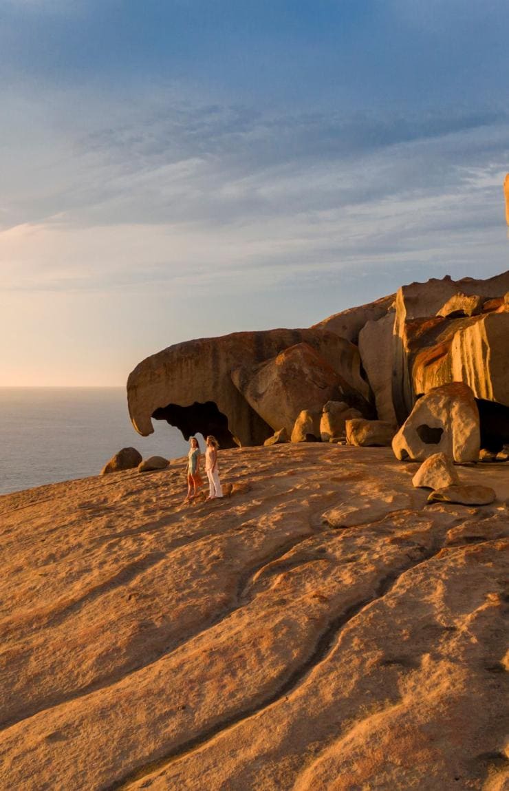 Hai người dạo bước bên những khối đá kỳ vĩ của Remarkable Rocks khi hoàng hôn buông xuống, phía sau là đại dương trên Đảo Kangaroo, tiểu bang Nam Úc © South Australian Tourism Commission