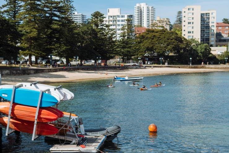 新南威尔士州,曼利镇,一排橙色的皮划艇沿着曼利镇皮划艇中心岸边一字排开,周围人们在划皮艇 © 新南威尔士州旅游局版权所有 新南威尔士州,曼利镇,一排橙色的皮划艇沿着曼利镇皮划艇中心岸边一字排开,周围人们在划皮艇 © 新南威尔士州旅游局版权所有