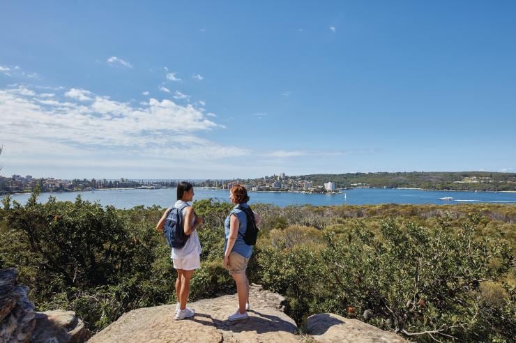 新南威尔士州,悉尼,在斯皮特桥至曼利镇步道上,两个人站在一块岩石上俯瞰着绿色植被和悉尼海港 © 新南威尔士州旅游局版权所有 新南威尔士州,悉尼,在斯皮特桥至曼利镇步道上,两个人站在一块岩石上俯瞰着绿色植被和悉尼海港 © 新南威尔士州旅游局版权所有